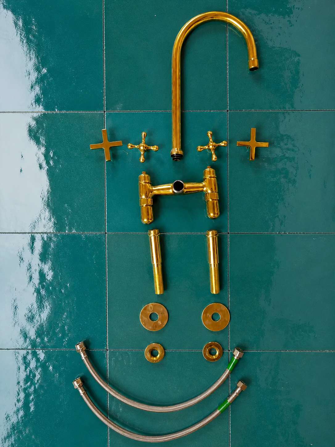 A brass faucet set laid out on glossy teal tiles, including a curved gooseneck spout, two cross-shaped handles, a central faucet body, two vertical pipe sections, two round washers, two small flat washers, and two metal supply hoses.