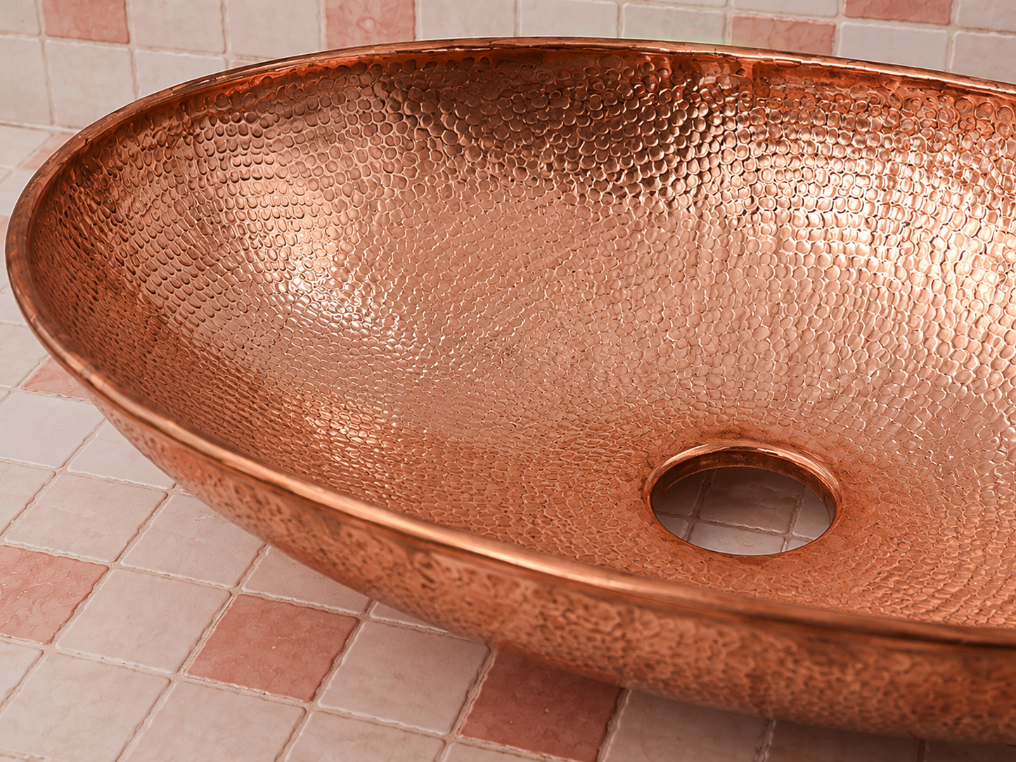 A hammered copper vessel sink basin with a textured metallic finish, shown on a pinkish-beige tiled surface.