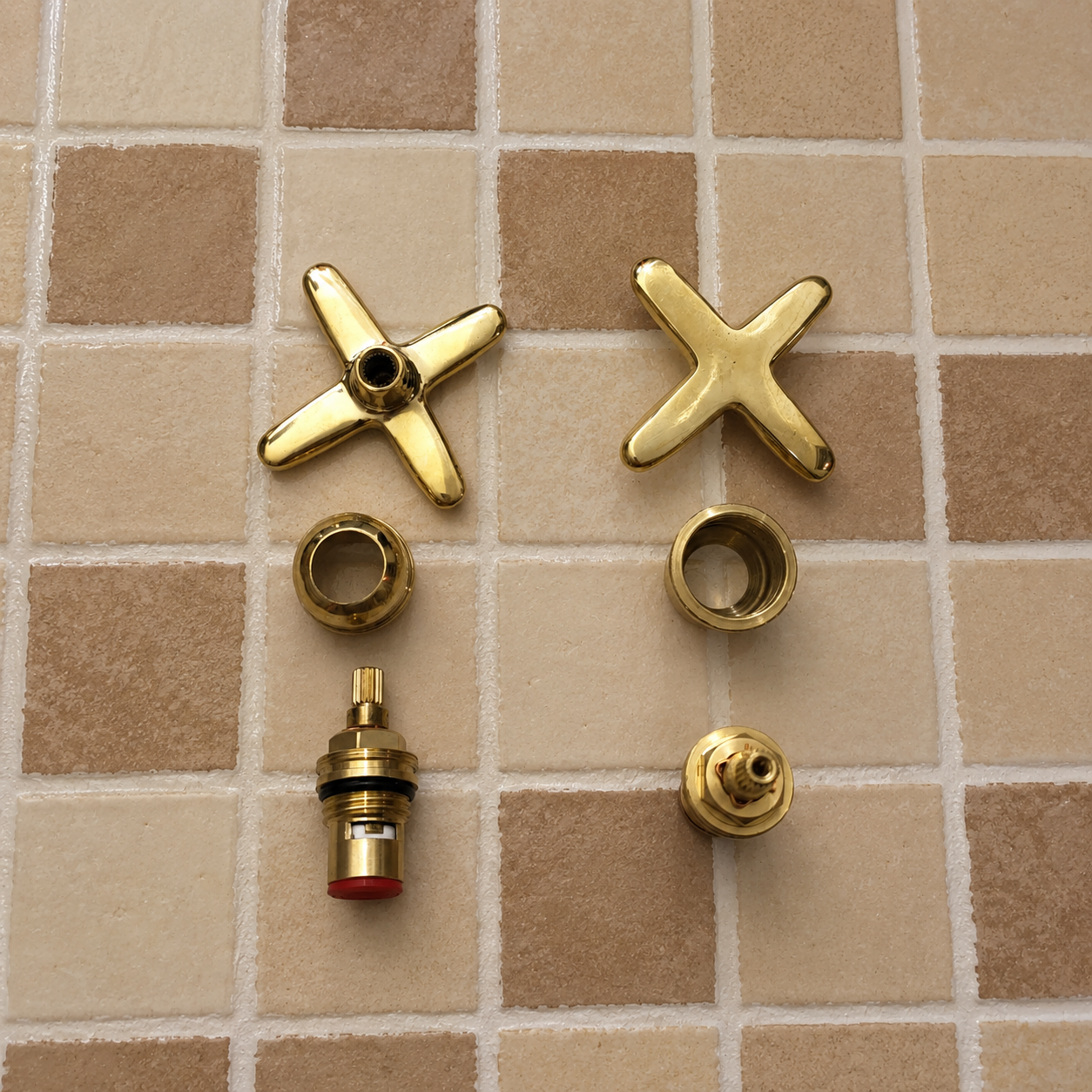 A set of brass bathroom faucet replacement parts, including two four-spoke star handles, two ring collars, and two valve seat assemblies, arranged on a beige tiled surface.
