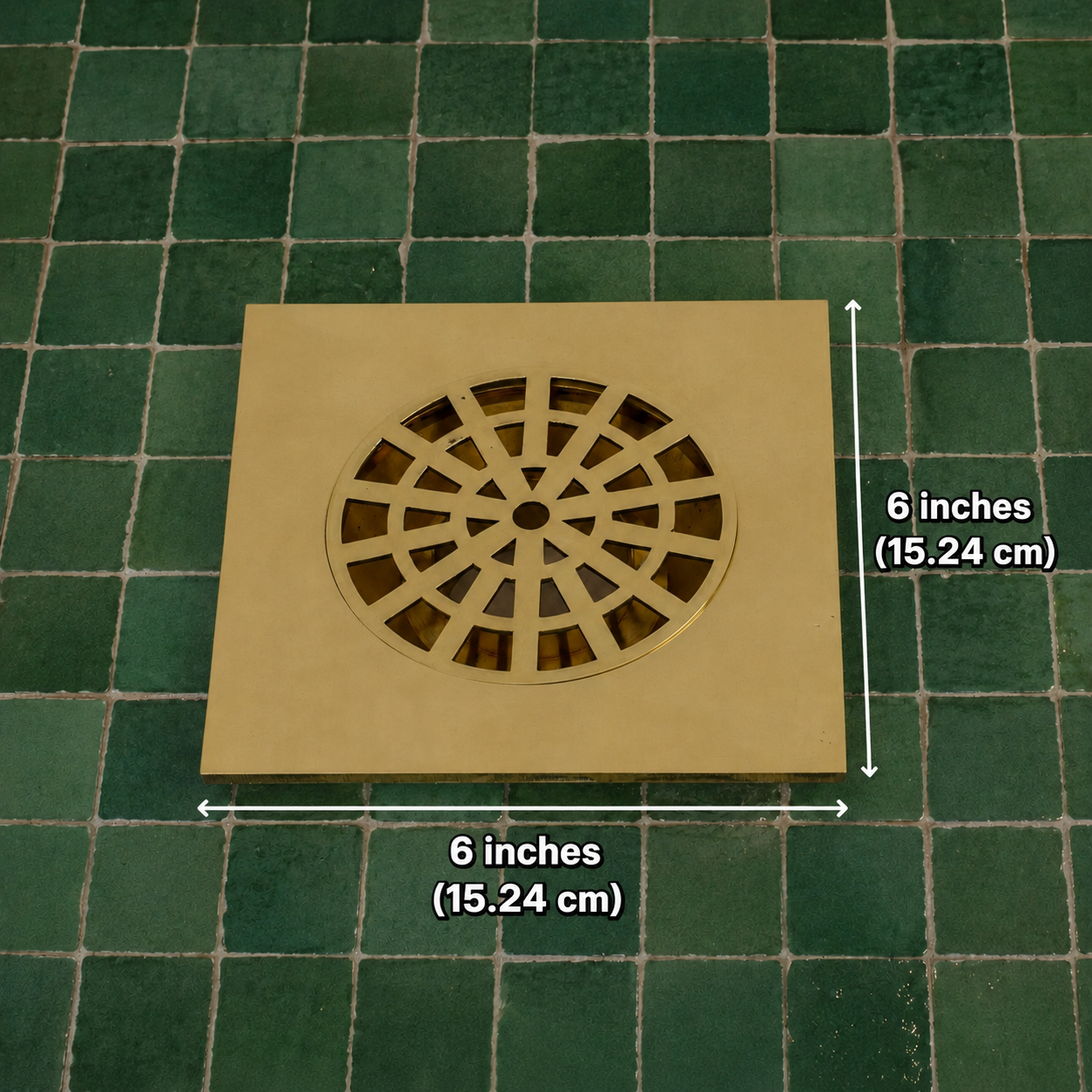 A square tan drain cover with a circular slotted center, shown on a green tiled floor with dimension arrows and text indicating 6 inches (15.24 cm) by 6 inches (15.