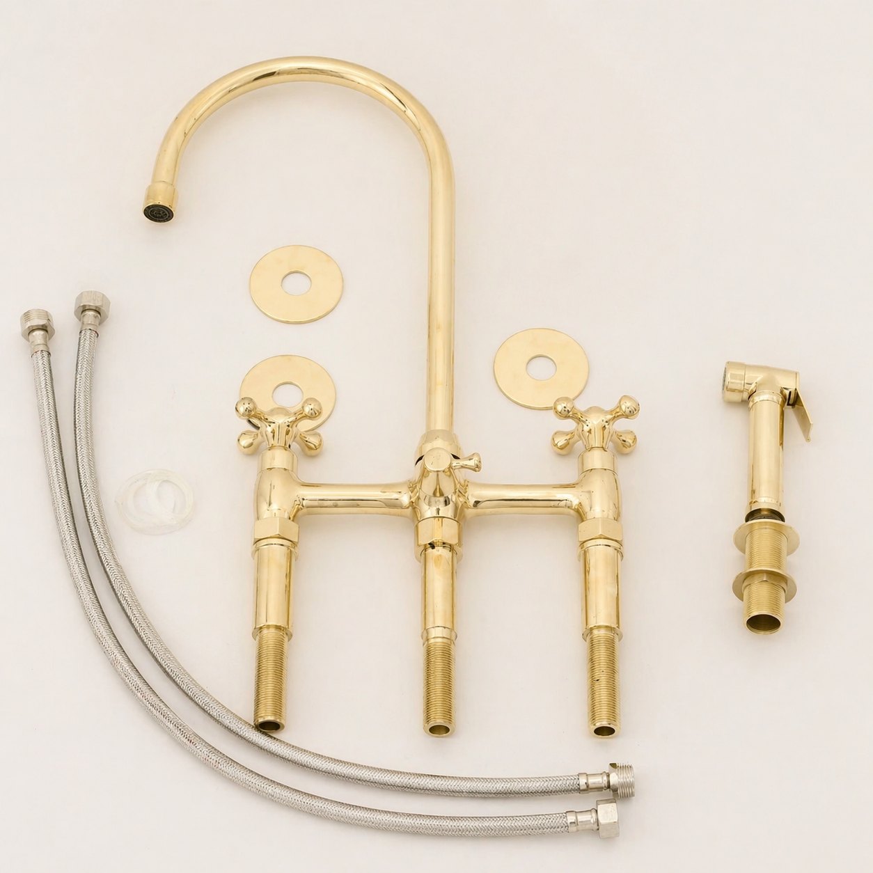 A brass three-hole faucet set with a tall curved spout, two cross-handle faucets, two round mounting plates, two braided steel supply hoses, and a separate handheld sprayer, all arranged on a plain white background.