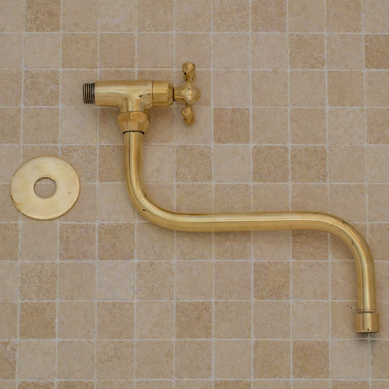 Handmade solid brass wall-mounted pot filler faucet with a swiveling neck and unlacquered living brass finish installed above a kitchen stove.