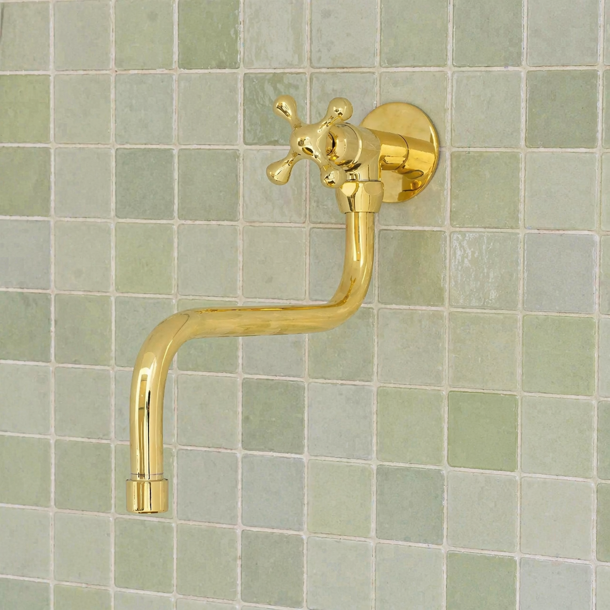Handmade solid brass wall-mounted pot filler faucet with a swiveling neck and unlacquered living brass finish installed above a kitchen stove.
