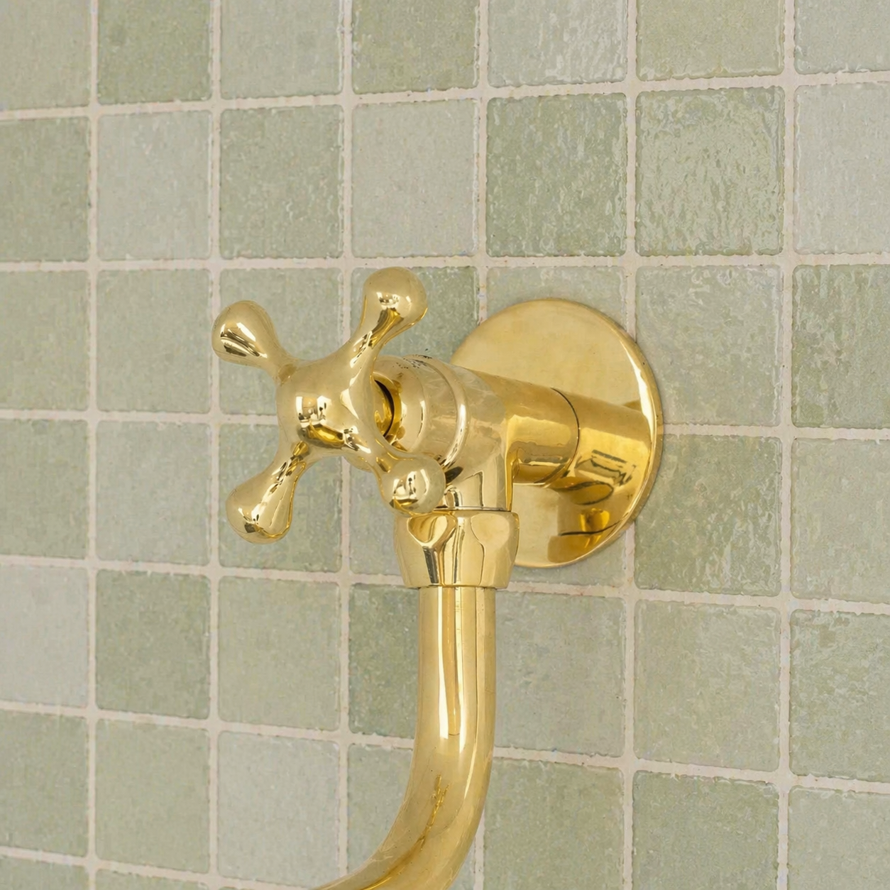 Handmade solid brass wall-mounted pot filler faucet with a swiveling neck and unlacquered living brass finish installed above a kitchen stove.
