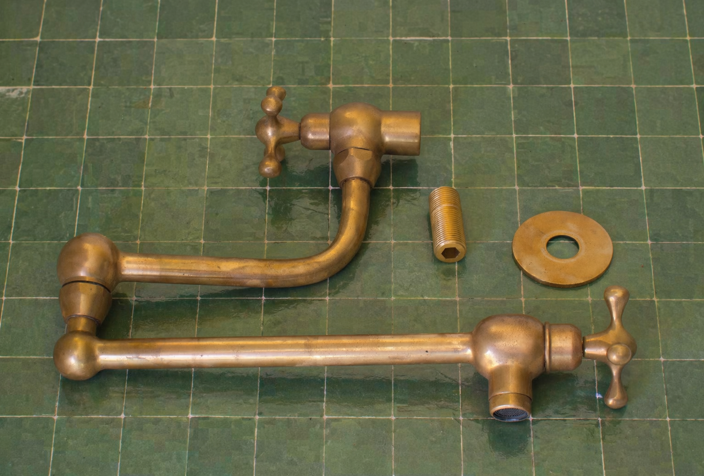 Handmade unlacquered solid brass wall-mounted pot filler faucet with double swing arms and dual shut-off valves installed above a kitchen stove.