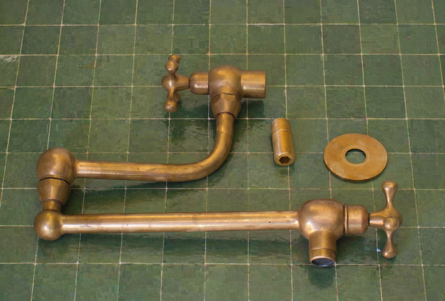 Handmade unlacquered solid brass wall-mounted pot filler faucet with double swing arms and dual shut-off valves installed above a kitchen stove.