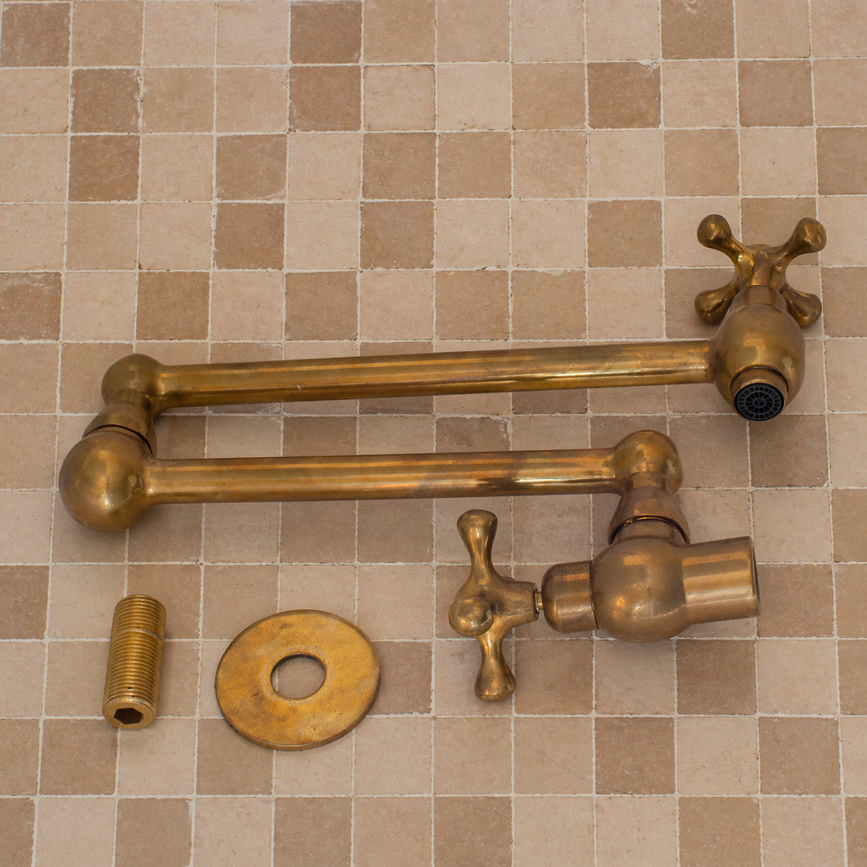 Handmade unlacquered solid brass wall-mounted pot filler faucet with dual swing arms and cross handles installed above a kitchen stove.