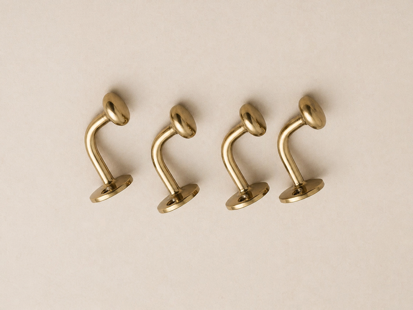 Four gold-plated curved barbell stud earrings arranged in a row on a light beige background.