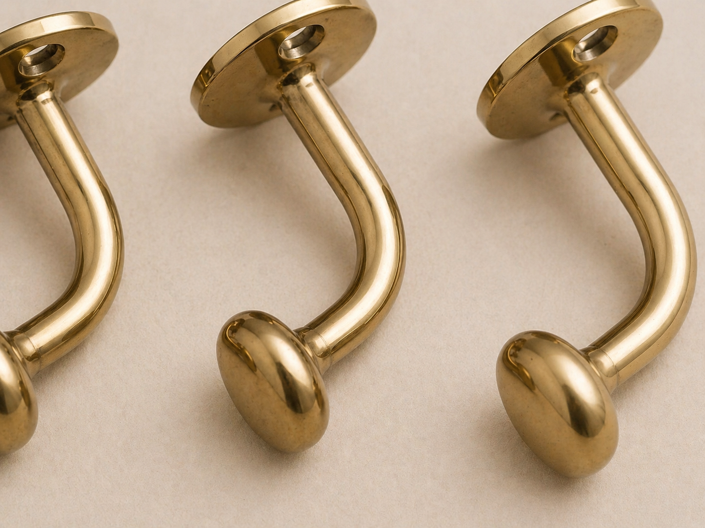Three polished gold-tone curved barbell studs with round ball ends and flat circular backing plates, arranged diagonally on a light beige surface.
