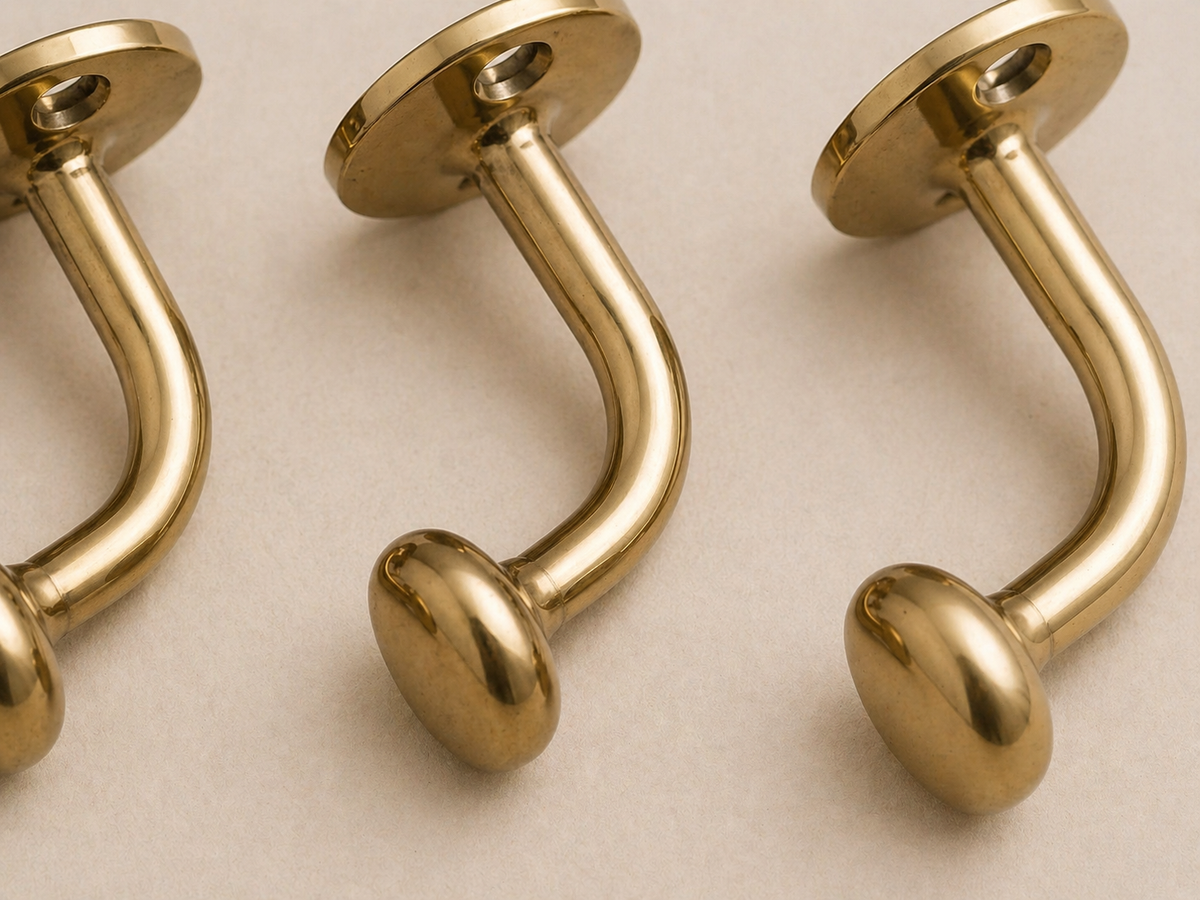 Three polished gold-tone curved barbell studs with round ball ends and flat circular backing plates, arranged diagonally on a light beige surface.