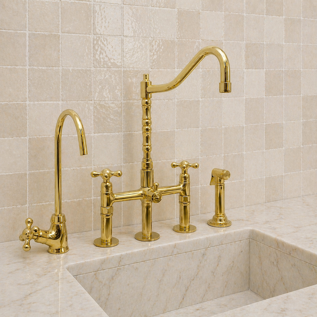 A polished gold brass bridge faucet set installed in a white marble sink, with a matching high-arc gooseneck spout, a separate hot water faucet, a side sprayer, and a tiled backsplash behind.