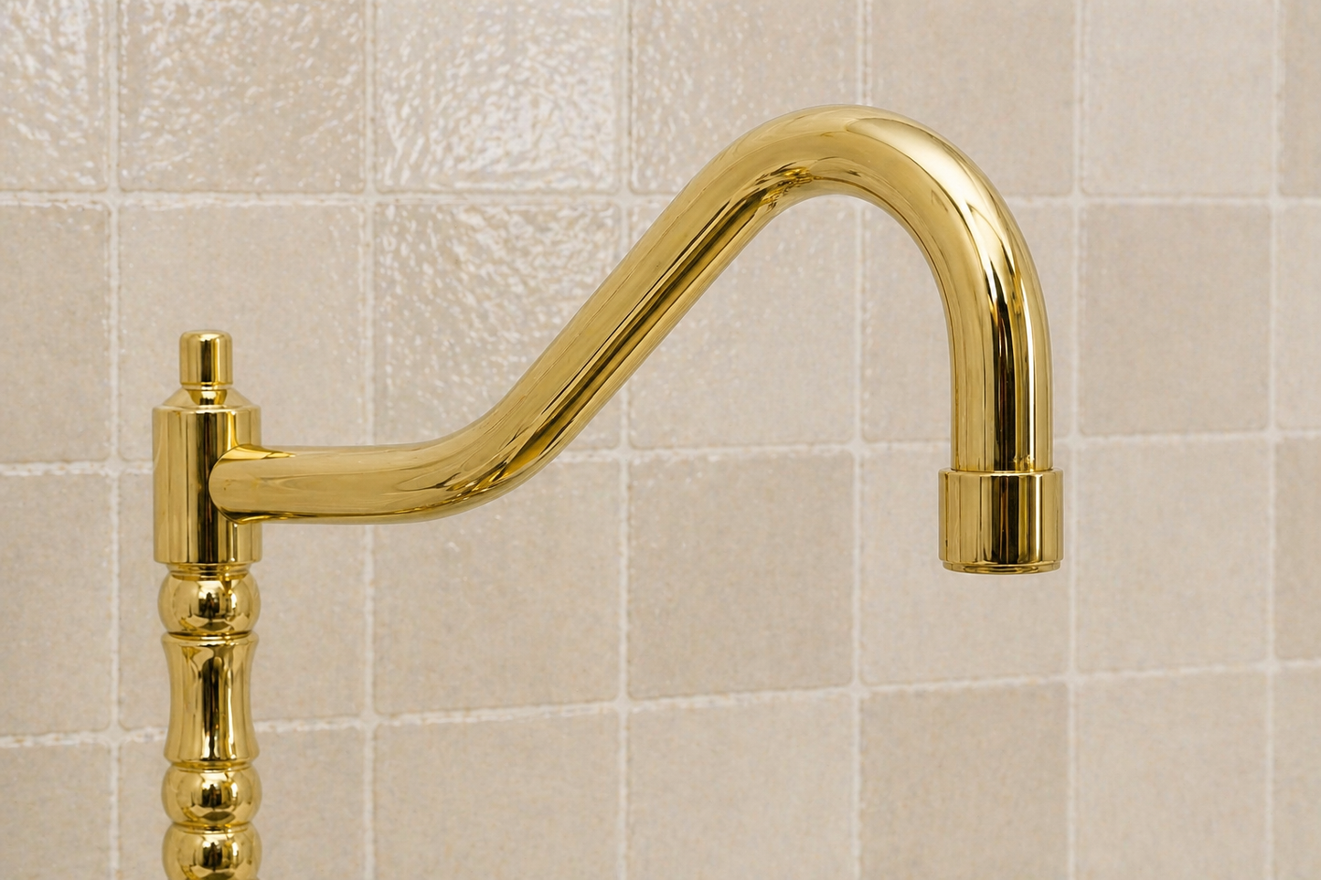 A polished gold wall-mounted faucet with a curved gooseneck spout and a decorative vertical handle, shown against a light beige tiled wall.