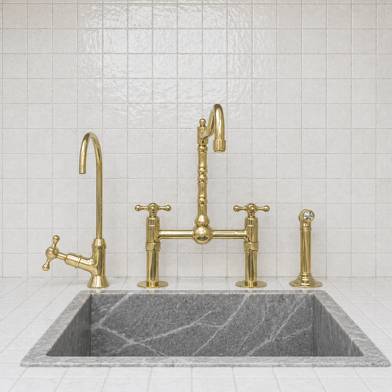 A polished brass kitchen faucet set installed over a dark gray marble sink, set against a white tiled backsplash.