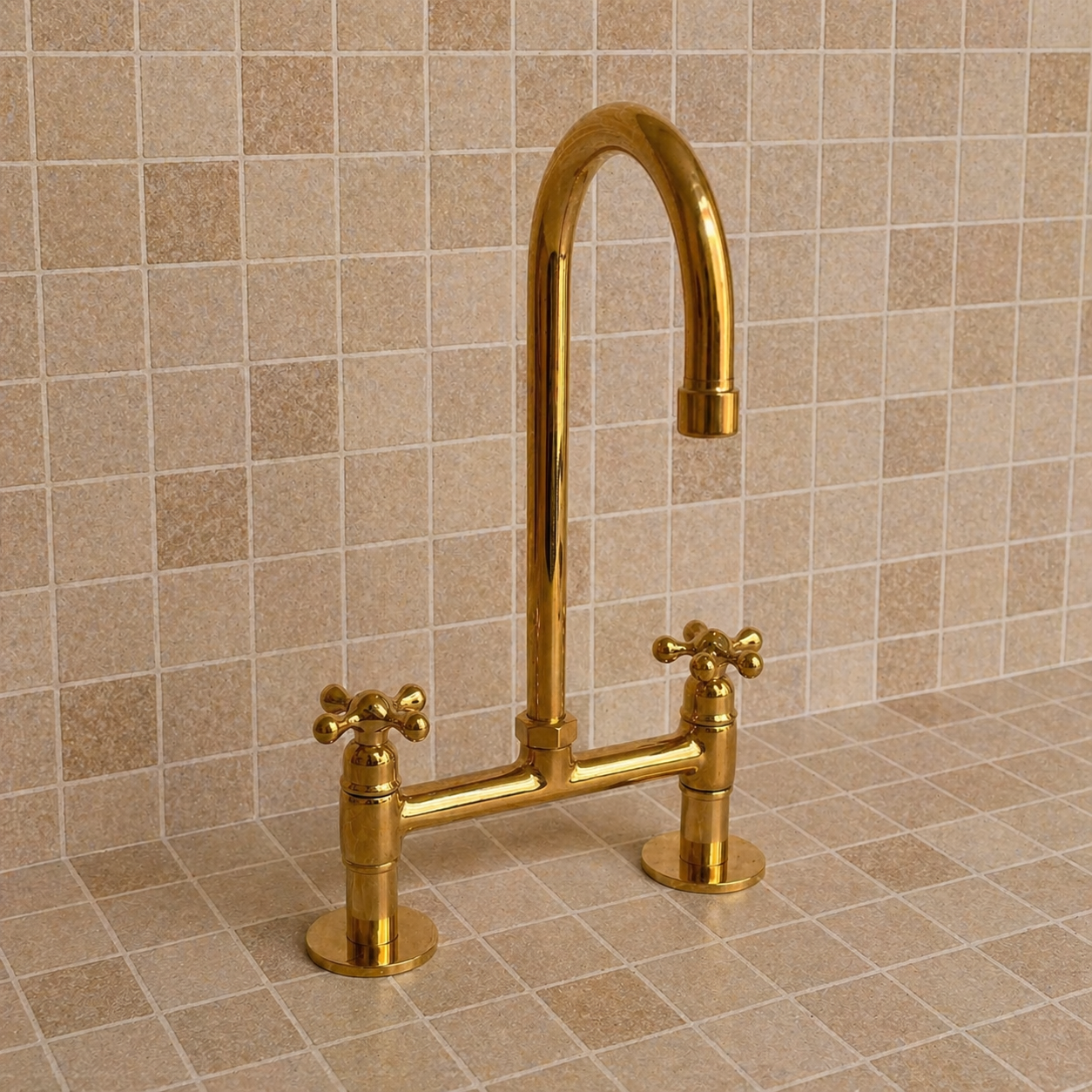 A polished gold bridge faucet with two cross handles and a high-arc spout, shown installed against a beige tiled backsplash and countertop.