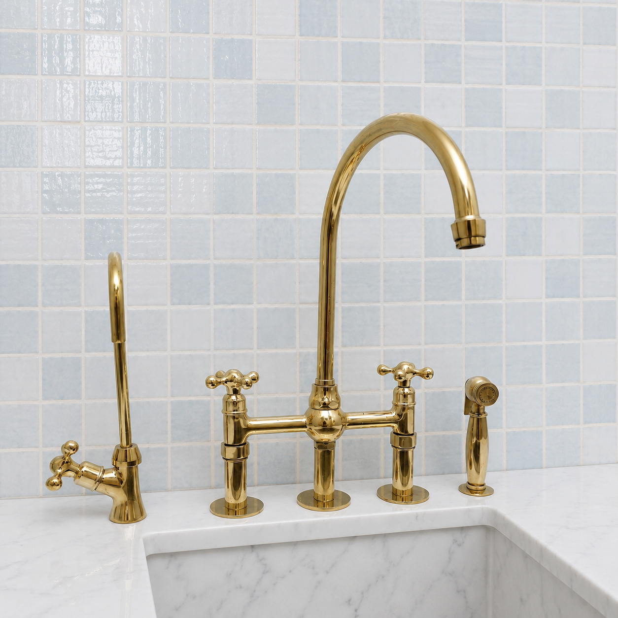 A polished brass bridge faucet set with a high-arc spout, cross handles, a side mixer, a tall side sprayer, and a handheld shower head, installed on a white marble sink against a light blue tiled backsplash.