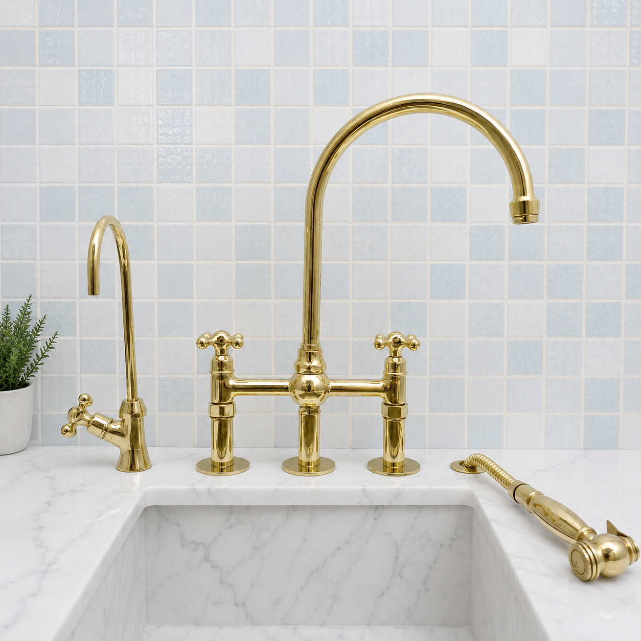 Gold-finished bridge faucet set with a high-arc main spout, separate hot and cold handles, a side pull-down sprayer, and a matching side faucet, installed on a white marble sink against a light blue mosaic tile backsplash.