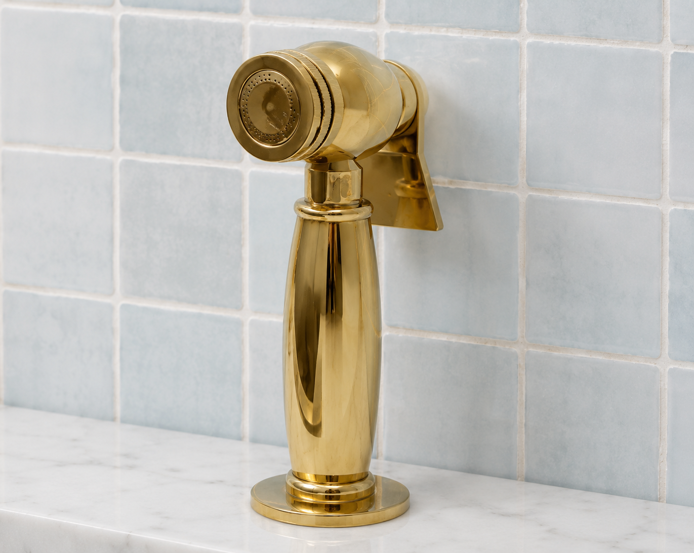 A polished brass garden hose sprinkler attachment mounted on a white marble ledge against a light blue tiled wall.