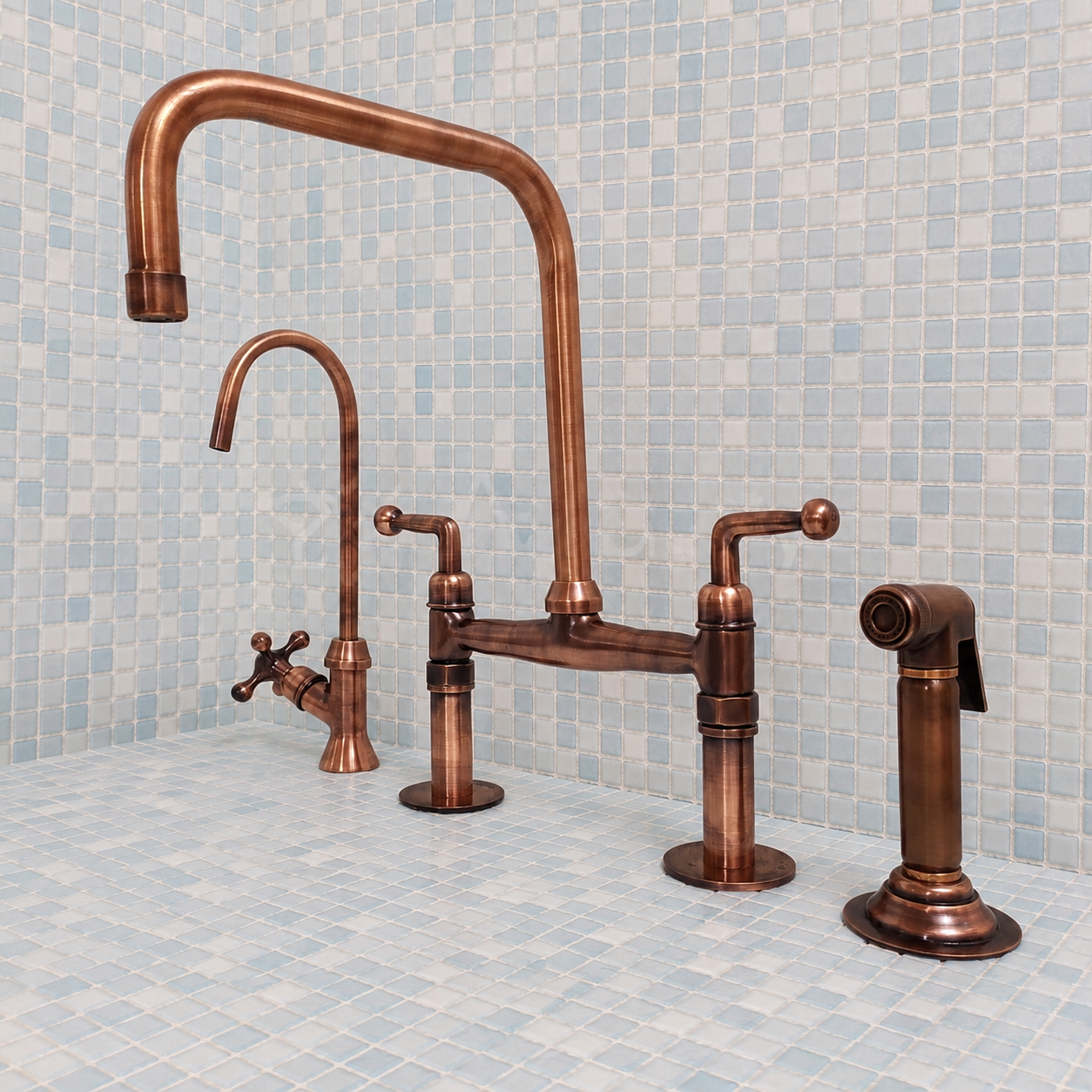 A three-hole bridge faucet set in a warm copper finish, featuring a high-arc main spout, a secondary curved spout with a cross handle, a central deck plate, and a separate side sprayer, set against a light blue mosaic tile wall and counter.