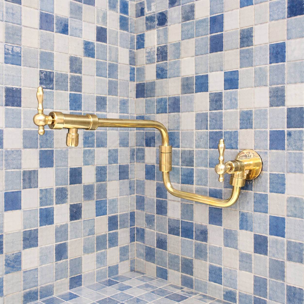 Handcrafted unlacquered solid brass wall mounted pot filler kitchen faucet with dual lever handles installed against blue tile backsplash