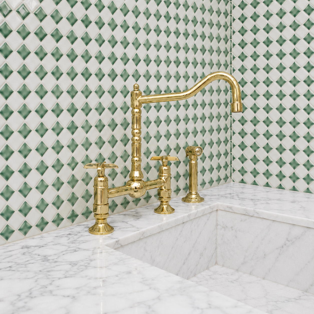 A polished brass bridge faucet with a high-arc spout and two cross-handle valves, installed on a white marble sink against a green and white diamond-patterned tile backsplash.