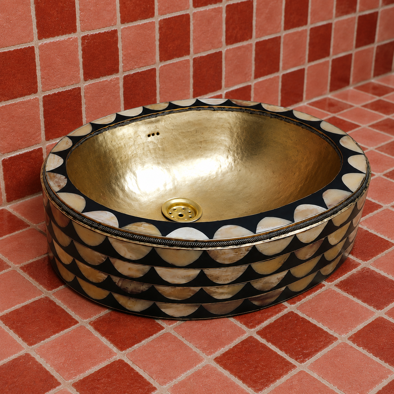 A round vessel sink with a hammered gold interior and a black exterior decorated with scalloped mother-of-pearl shell patterns, set against a red tiled background.