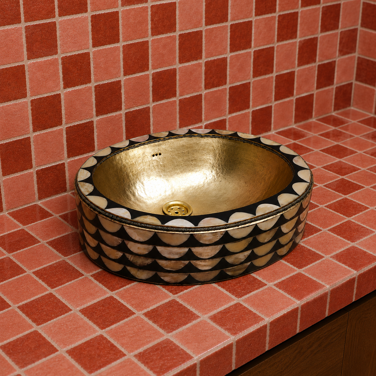 A round vessel sink with a hammered gold interior and a black-and-white scalloped shell-look exterior, set into a coral tile countertop and backsplash.