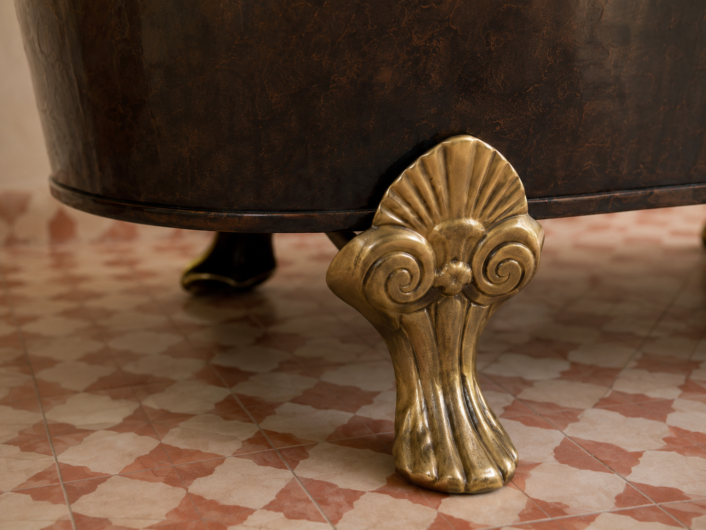 Close-up of an ornate antique-style brass clawfoot leg attached to a dark brown metal tub, set on a red and cream checkered tile floor.