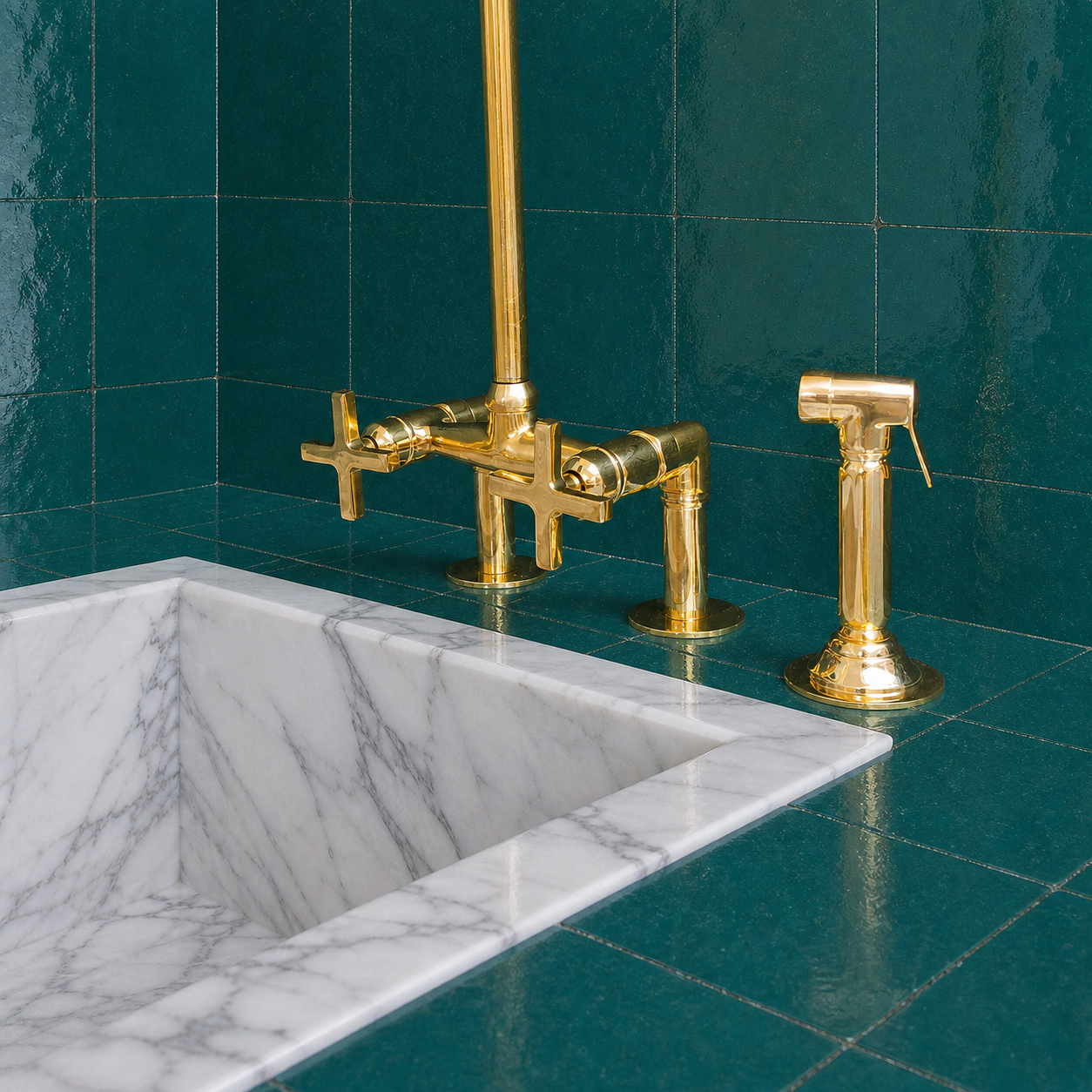A polished gold brass faucet set with a cross-handle main spout and a separate handheld shower sprayer, installed beside a white marble sink on a teal tiled countertop.