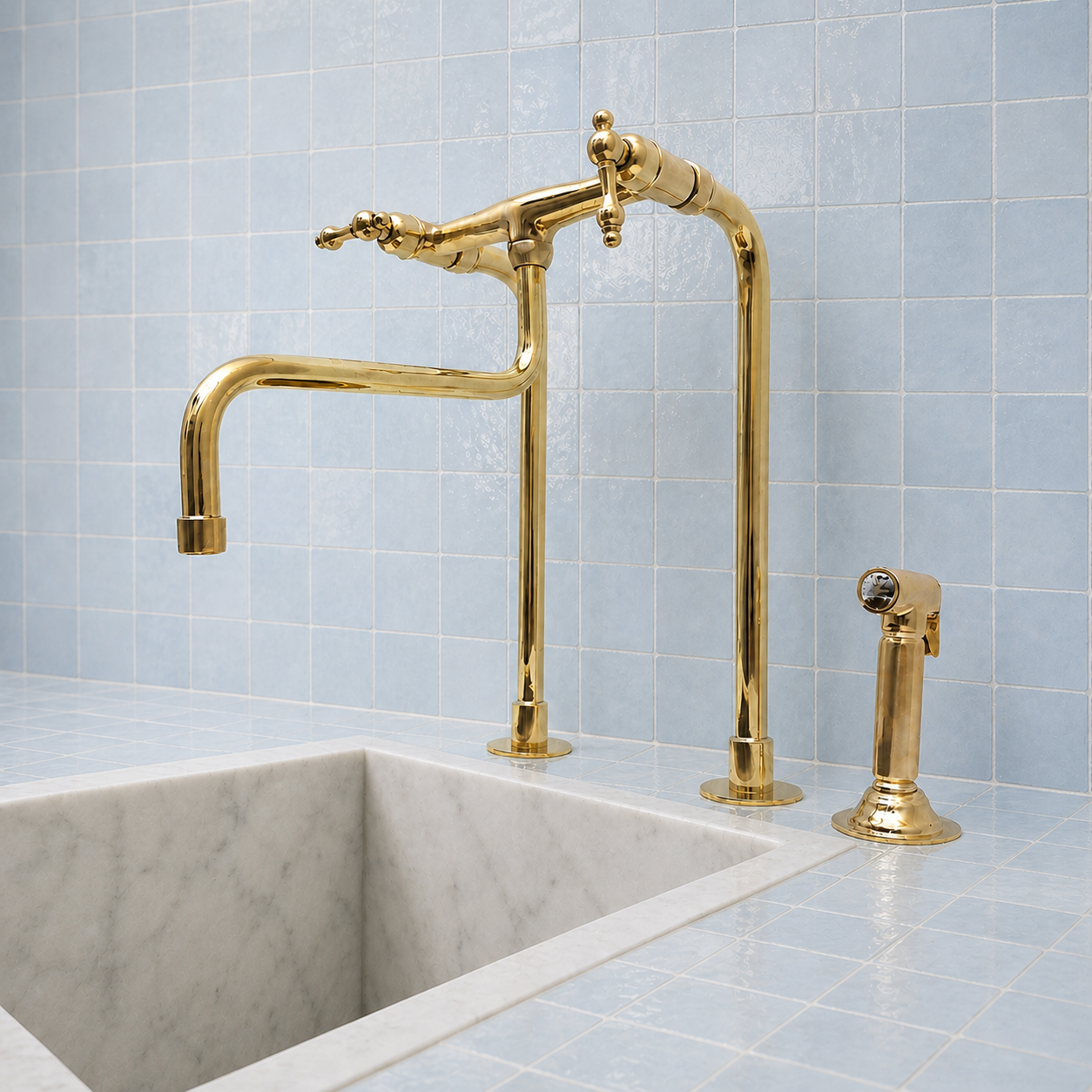 A polished brass kitchen faucet set with a high-arc gooseneck spout and a matching side sprayer, installed on a white marble sink against a light blue tiled backsplash.