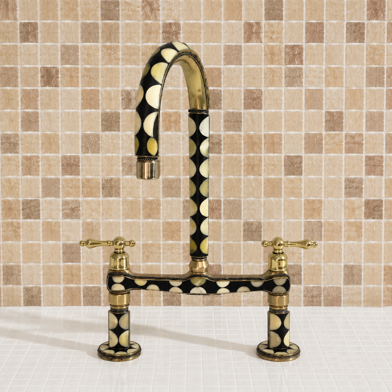 A bridge-style kitchen faucet with a curved gooseneck spout and two cross handles, featuring a black and gold polka-dot pattern with brass-toned hardware, set against a beige mosaic tile backsplash.