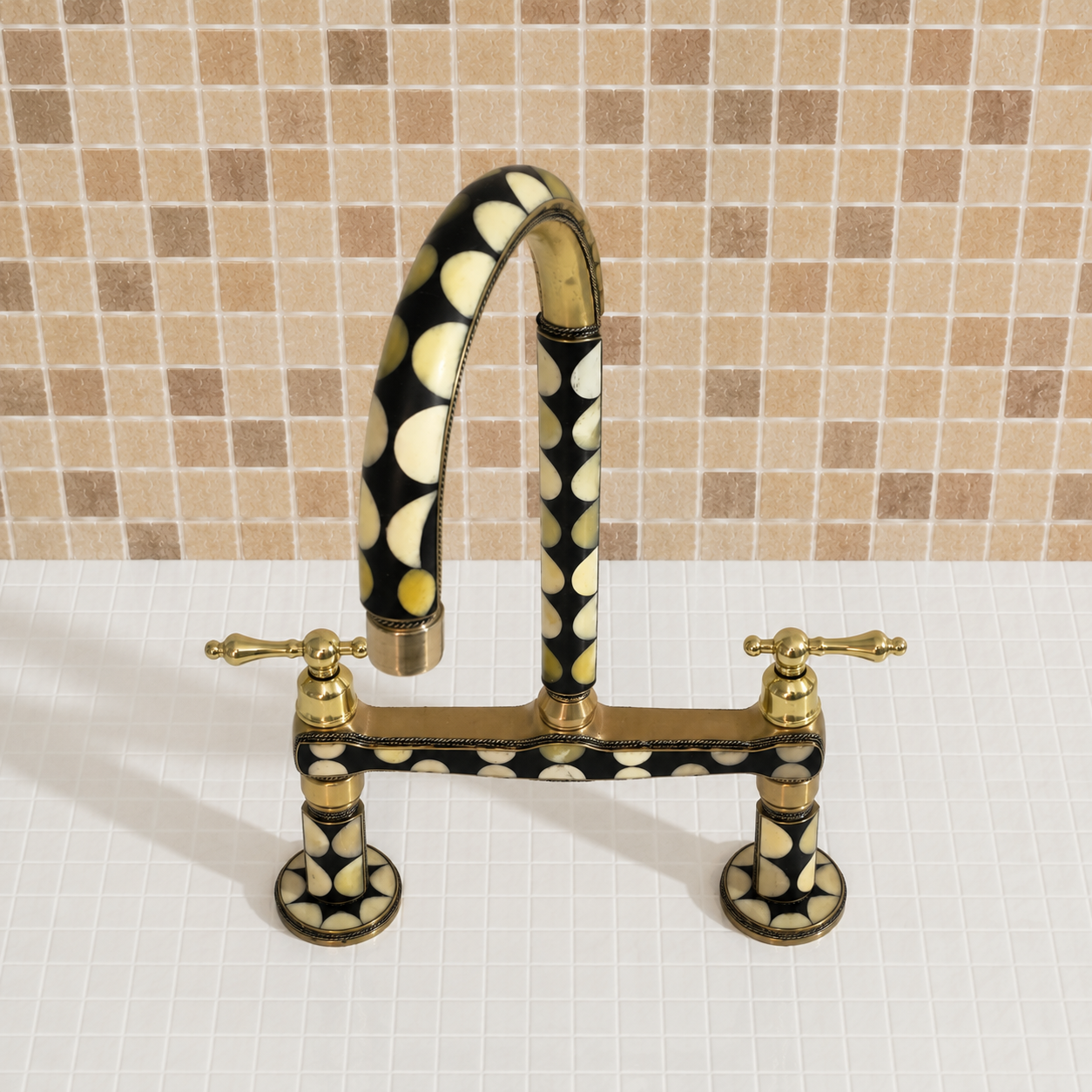 A bridge-style kitchen faucet with a curved gooseneck spout and two cross handles, featuring a black and cream polka-dot pattern with gold-toned metal accents, set against a beige mosaic tile backsplash.