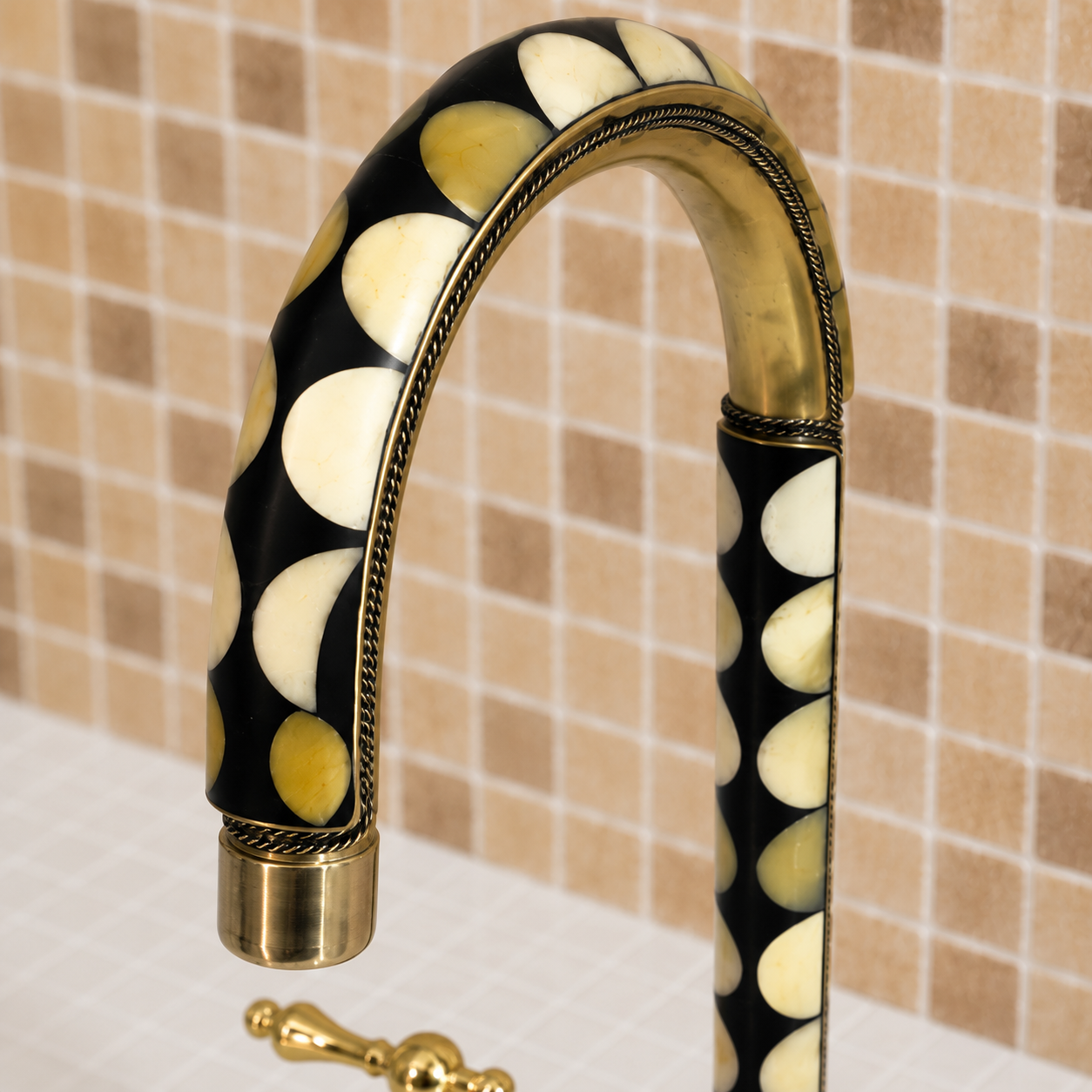 A close-up of a curved bathroom faucet with a black and cream bone-inlay handle and gold brass accents, set against a beige tiled wall.