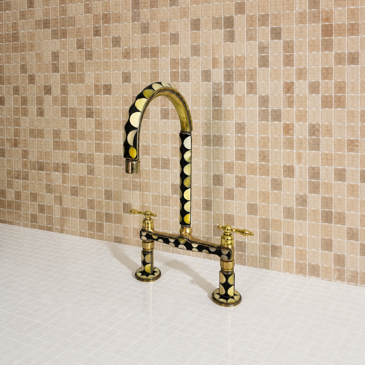 A bridge-style kitchen faucet with a curved gooseneck spout and two separate handles, finished in polished gold with black and yellow circular inlay detailing, set against a beige mosaic tile backsplash.