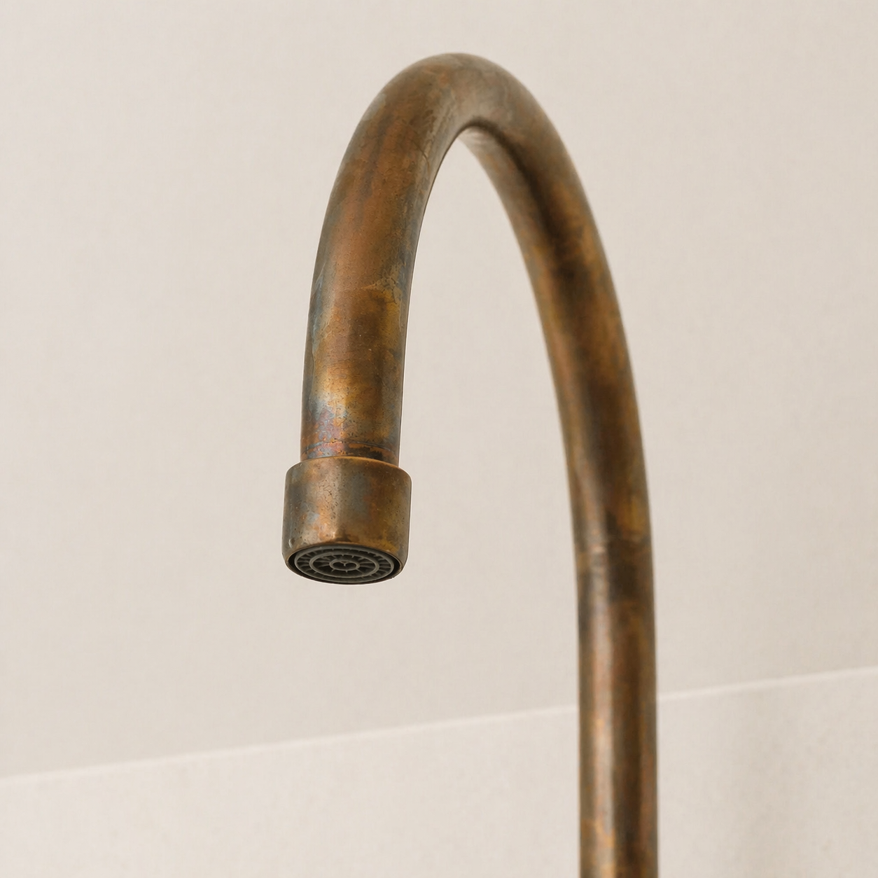 Close-up of high-arc spout and aerator on an aged brass bridge kitchen faucet