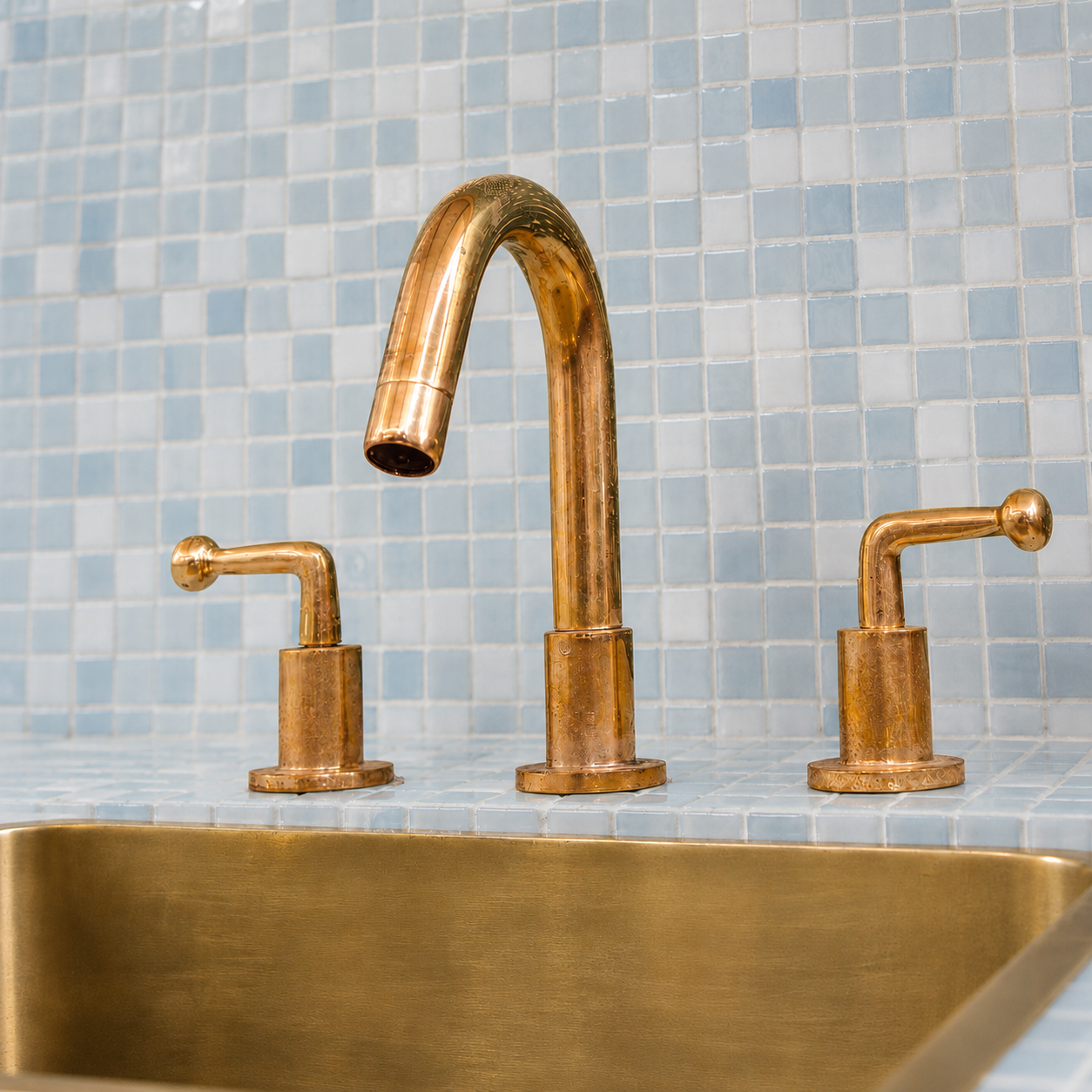 Front perspective of unlacquered brass bathroom faucet installed on a blue tiled vanity