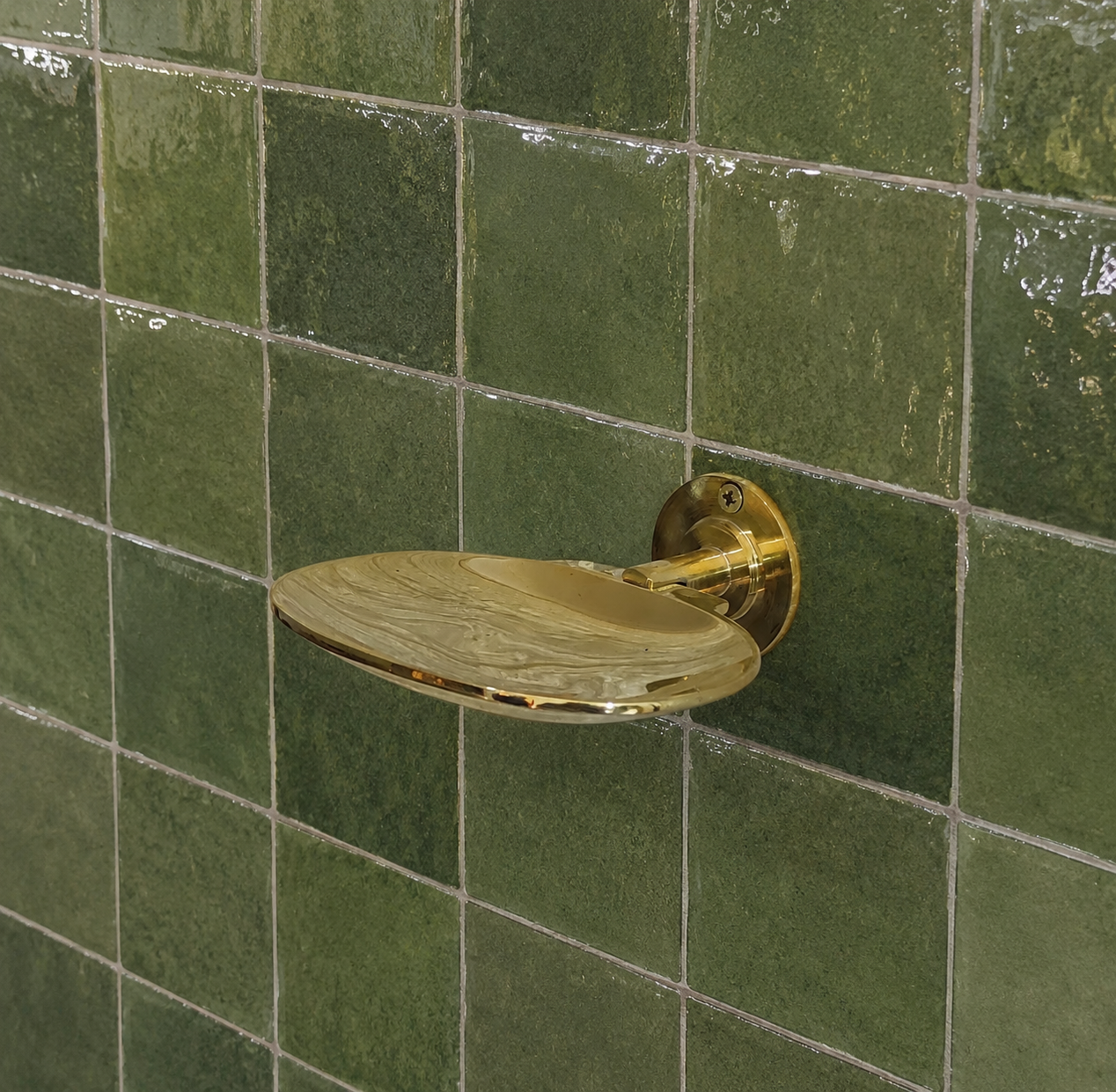 Handcrafted solid brass wall mounted soap holder with polished finish installed on a green tiled bathroom wall.