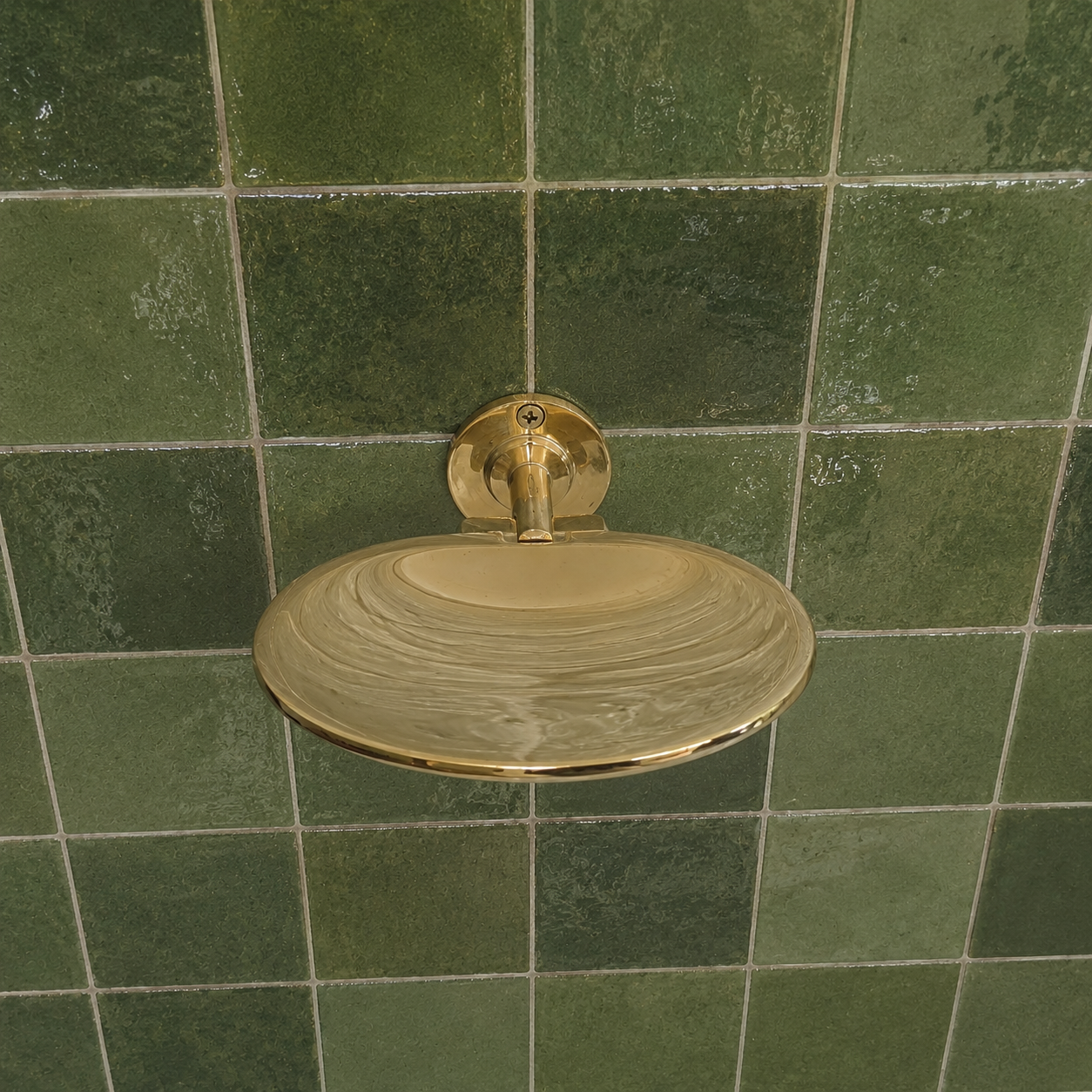 Handcrafted solid brass wall mounted soap holder with polished finish installed on a green tiled bathroom wall.