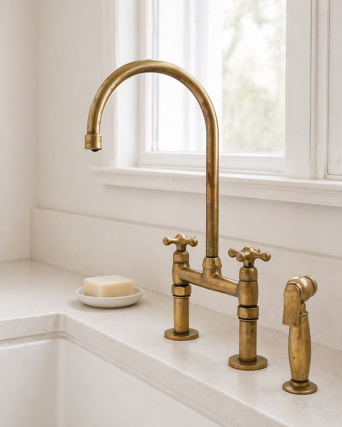 Unlacquered brass bridge kitchen faucet with matching side sprayer over a white farmhouse sink