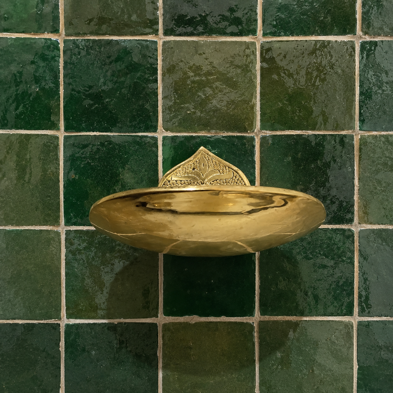 Handcrafted solid brass wall mounted soap holder with polished finish installed on a green tiled bathroom wall.