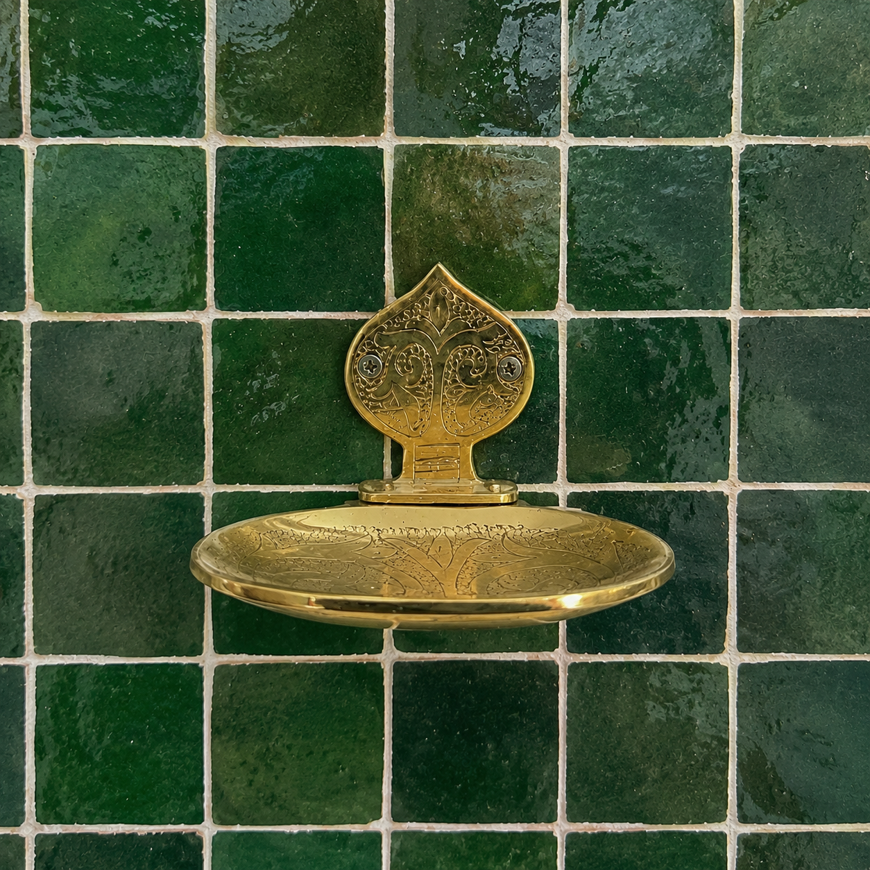 Handcrafted solid brass wall mounted soap holder with polished finish installed on a green tiled bathroom wall.