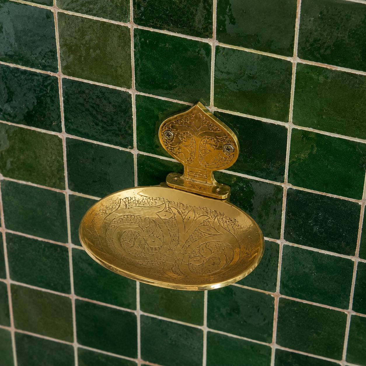 Handcrafted solid brass wall mounted soap holder with polished finish installed on a green tiled bathroom wall.