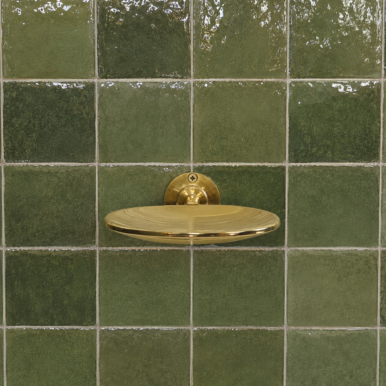 A polished gold metal soap dish mounted on a wall of glossy green ceramic tiles.