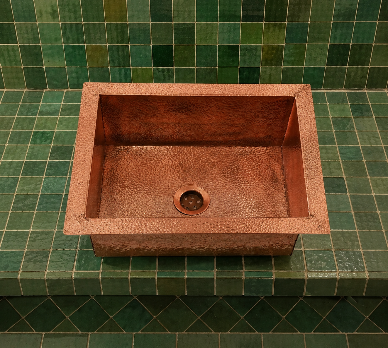 Handcrafted German silver round vessel sink with hammered polished basin and square surround in a Moroccan tiled bathroom