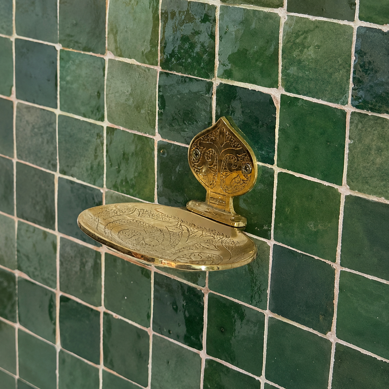 Handcrafted solid brass wall mounted soap holder with polished finish installed on a green tiled bathroom wall.