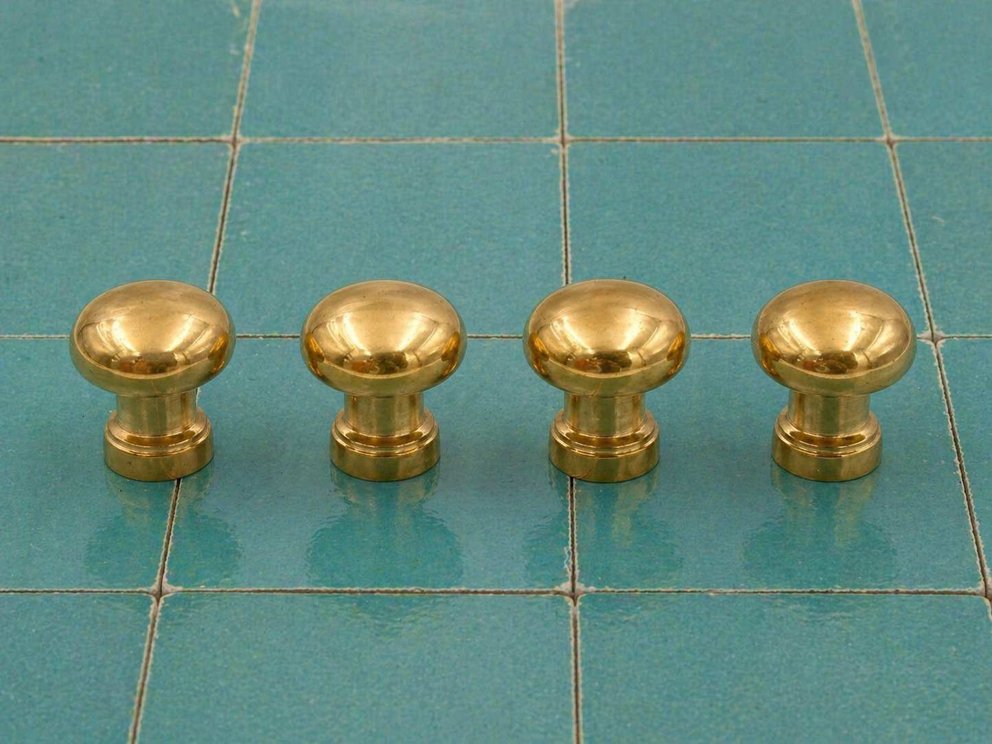 Four round brass cabinet knobs arranged in a row on a teal tiled surface.