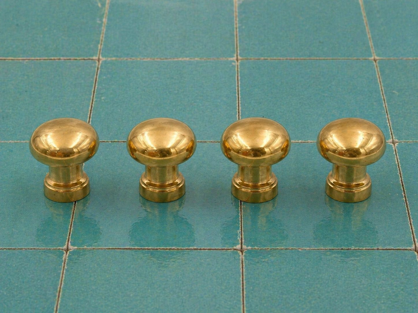 Four round brass cabinet knobs arranged in a row on a teal tiled surface.