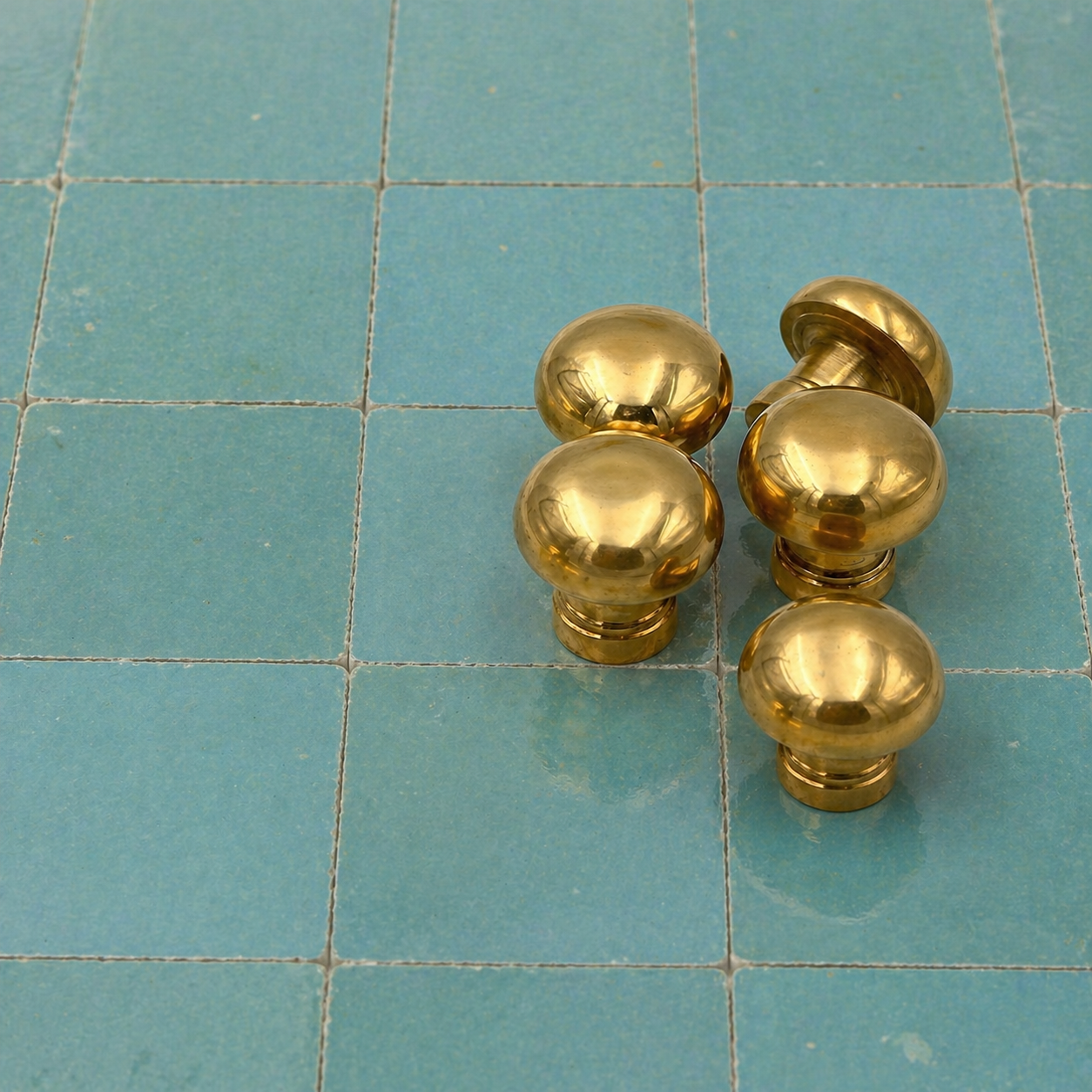 Four shiny brass round cabinet knobs arranged on a teal tiled surface.