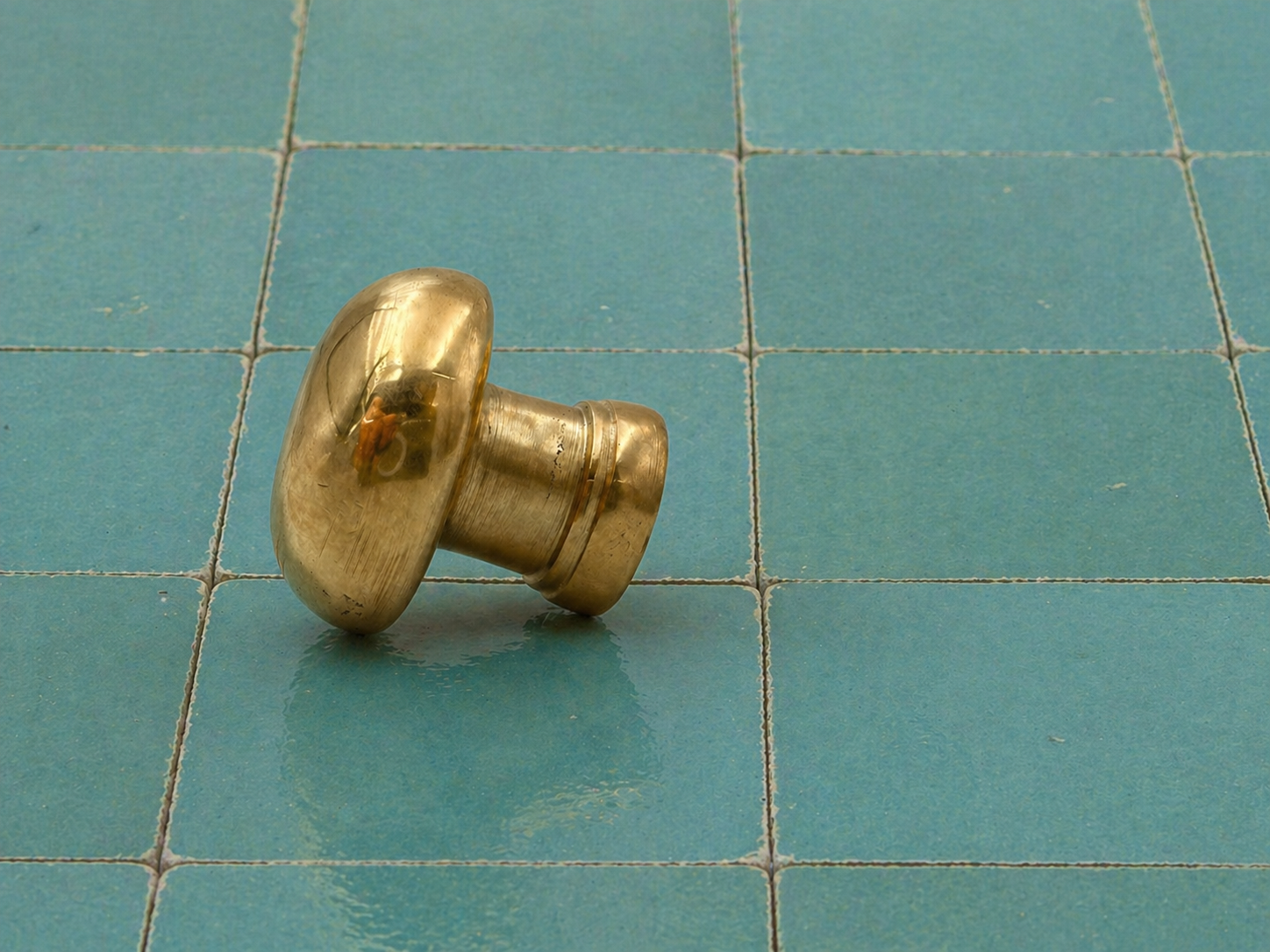 A small metallic brass knob or decorative hardware piece resting on a teal tiled surface.