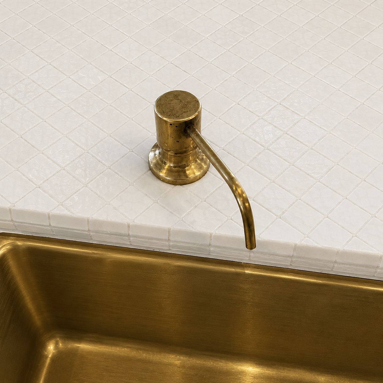 Handcrafted solid brass built-in sink soap dispenser installed on a countertop beside a brass kitchen sink.