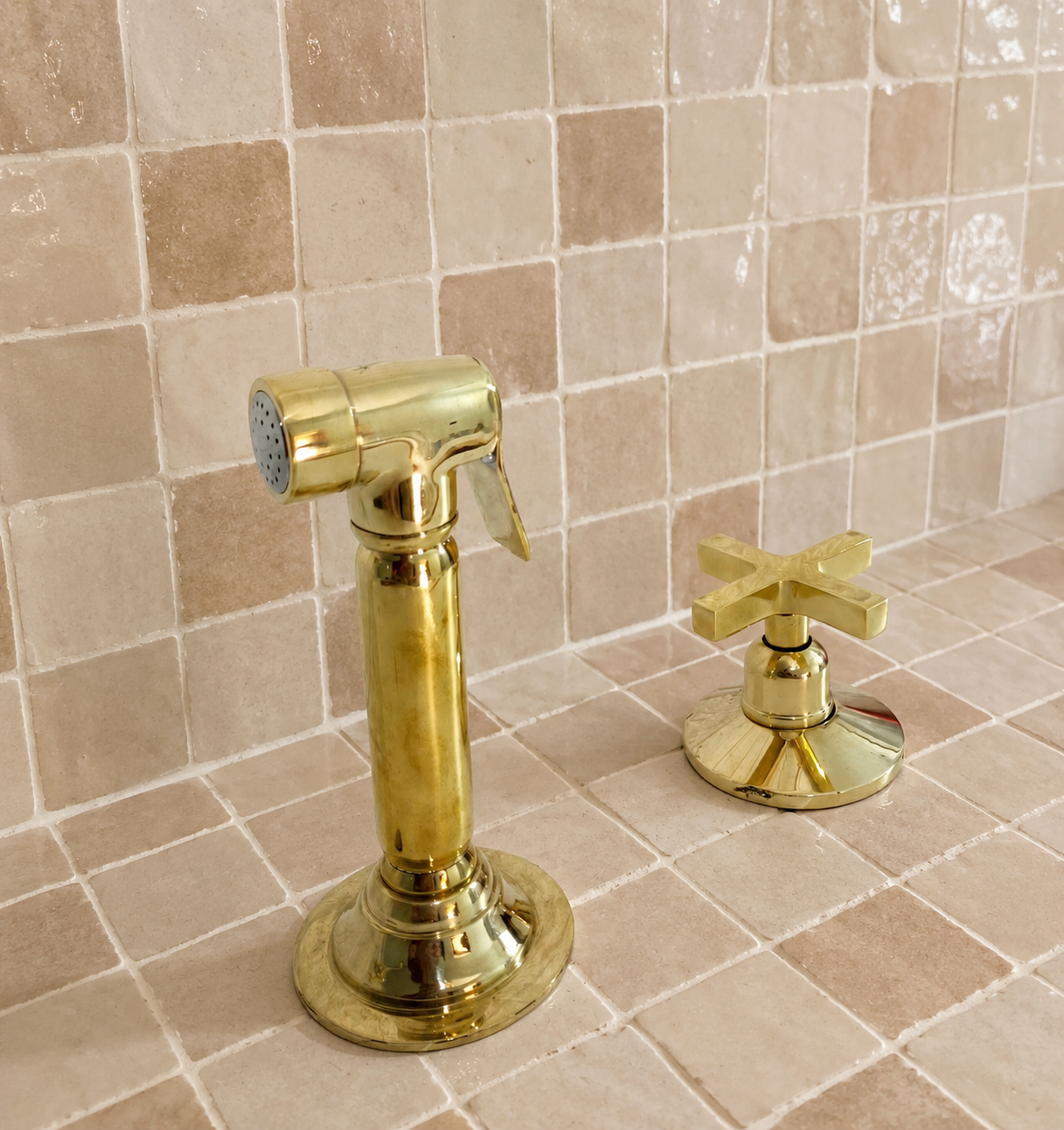 Handmade solid brass kitchen side sprayer with unlacquered finish and shut-off handle installed beside a kitchen faucet.